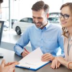 A couple is signing paperwork at a Buy Here Pay Here dealership.