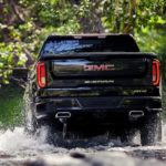 A black 2019 GMC Sierra is shown driving through a puddle from behind in the woods.