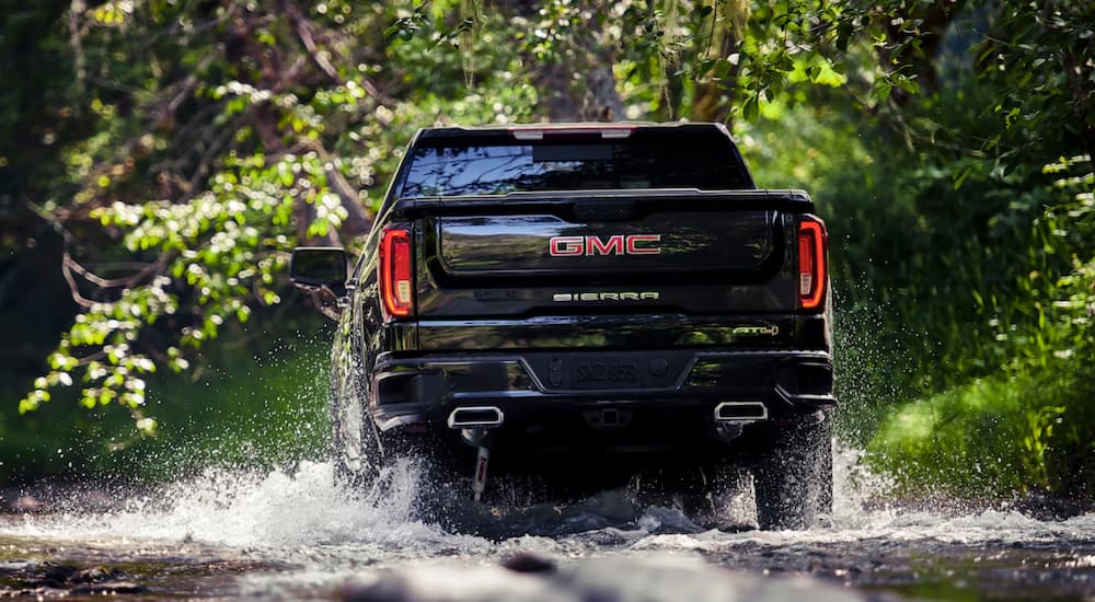 A black 2019 GMC Sierra is shown driving through a puddle from behind in the woods.