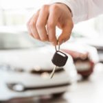 A closeup of a hand holding keys at a used car dealer is shown.