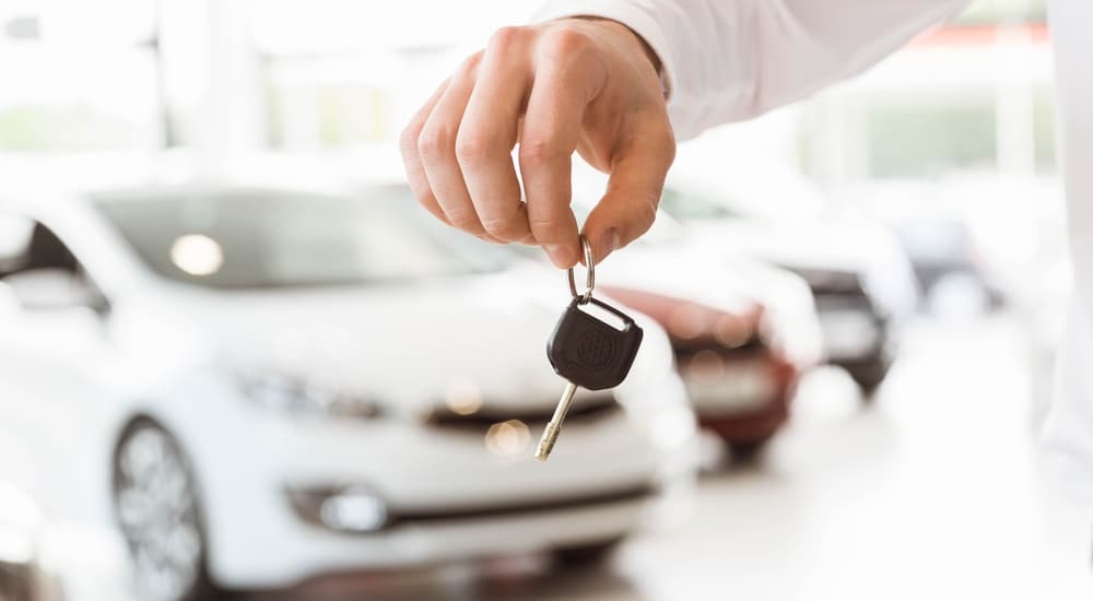 A closeup of a hand holding keys at a used car dealer is shown.
