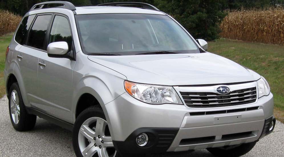A silver 2010 Subaru Forester is shown parked near the woods with trees in the background.