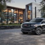 A black 2019 GMC Acadia is parked in front of a glass building.