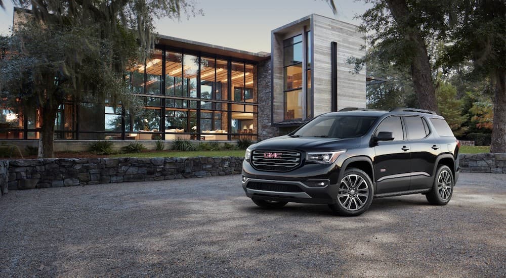 A black 2019 GMC Acadia is parked in front of a glass building.