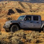 A grey 2020 Jeep Gladiator is driving in the desert with mountains in the background.