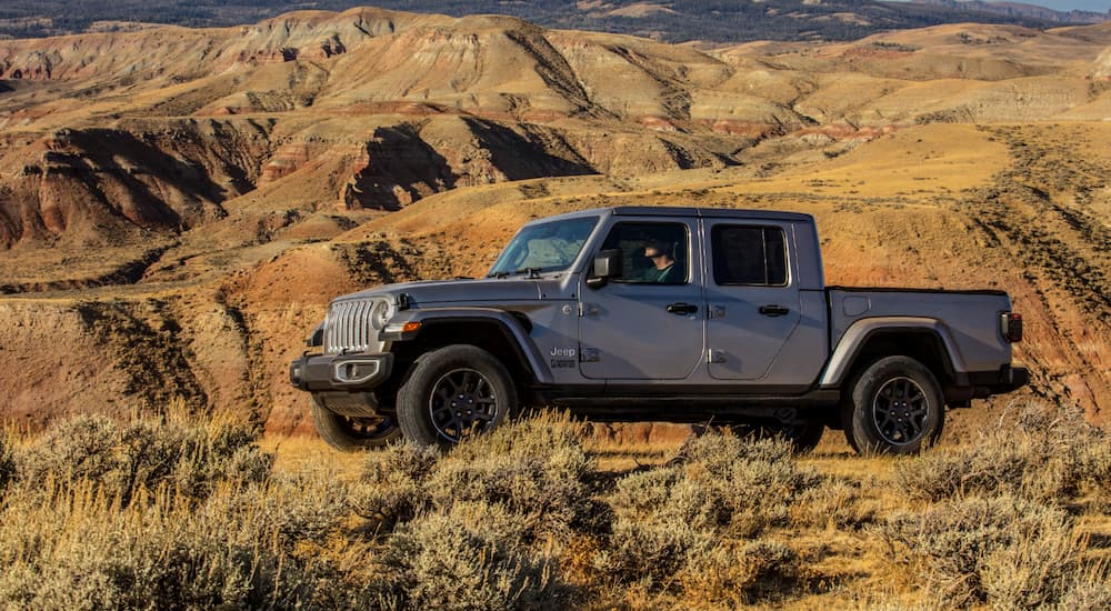 A grey 2020 Jeep Gladiator is driving in the desert with mountains in the background.