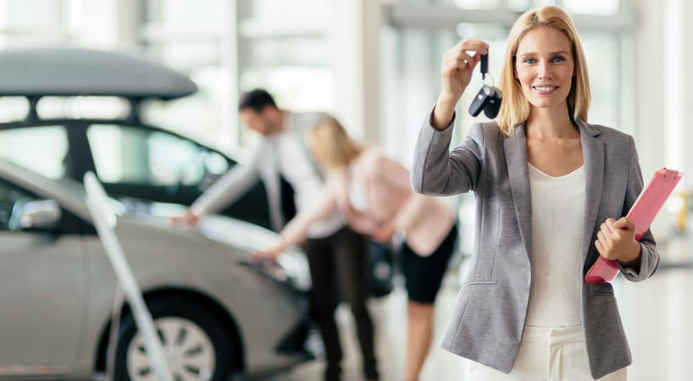 A sales woman is holding the keys to a car the couple behind her is looking at in a Buy Here Pay Here dealership.