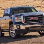 A grey 2015 GMC Sierra, popular among used trucks, is parked in front of a dry field.