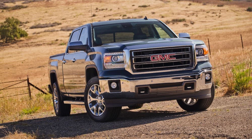 A grey 2015 GMC Sierra, popular among used trucks, is parked in front of a dry field.