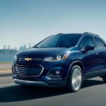 A blue 2019 Chevy Trax is driving away from a city.