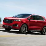 A red 2019 Ford Edge ST is taking a corner with a city skyline in the distance.