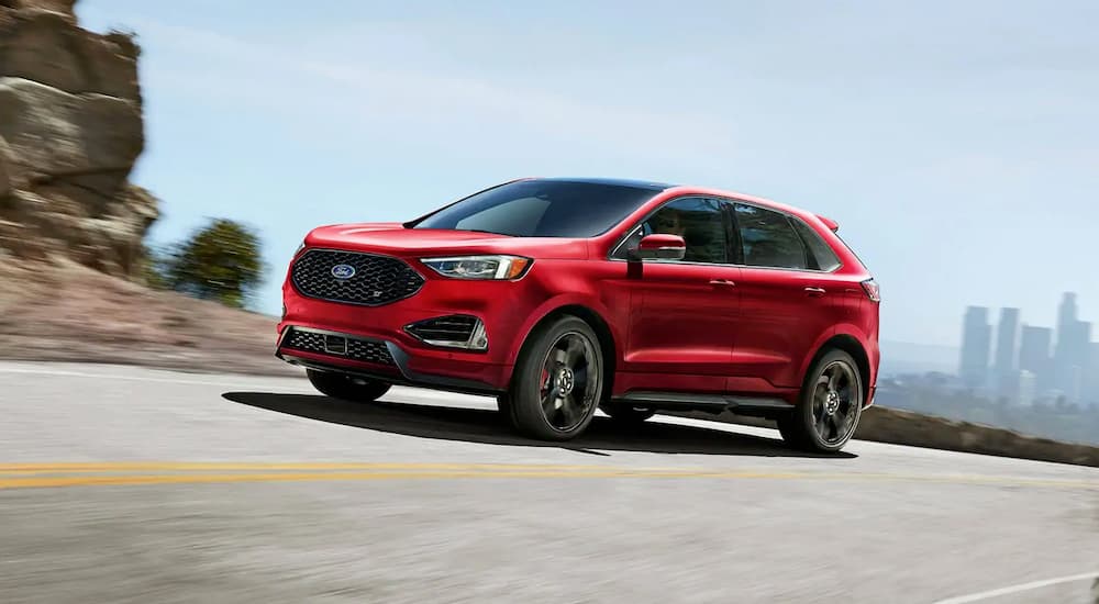 A red 2019 Ford Edge ST is taking a corner with a city skyline in the distance.