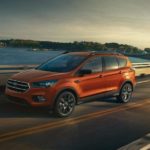 An orange 2019 Ford Escape is driving down a highway with a city in the background.
