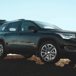 A man with a backpack is closing the trunk of his 2019 black GMC Acadia.
