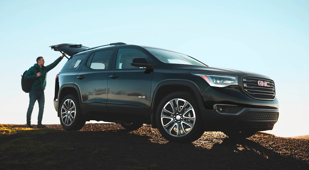 A man with a backpack is closing the trunk of his 2019 black GMC Acadia.