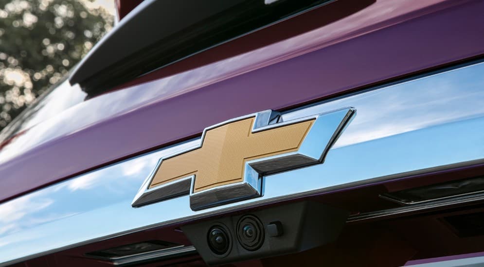 A close up of the Chevy logo is shown on a car at a Chevy dealership