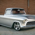 A silver 1957 Chevrolet 3100 Custom Pickup, one of the possible style vehicles at the NSRA 50th Annual Street Rod Nationals in Louisville KY, is parked in front of a brick wall.