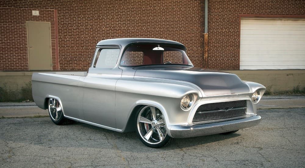 A silver 1957 Chevrolet 3100 Custom Pickup, one of the possible style vehicles at the NSRA 50th Annual Street Rod Nationals in Louisville KY, is parked in front of a brick wall.