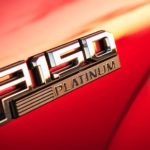 A closeup of a Ford F-150 Platinum emblem is shown on a red body panel.