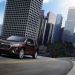 A burgundy 2019 Chevy Traverse is driving out of the city.