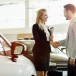 A saleswoman is shaking a customer's hand at a used car dealership.