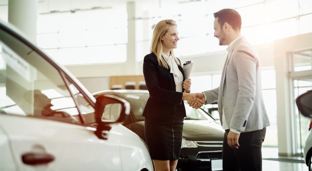 A saleswoman is shaking a customer's hand at a used car dealership.