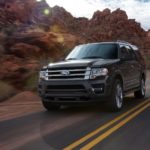 A black 2016 Ford Expedition is driving past red rocks.