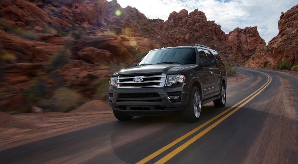 A black 2016 Ford Expedition is driving past red rocks.