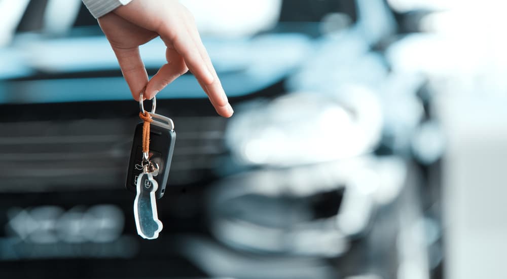 A closeup of someone holding keys to the used SUV for sale in the background is shown.