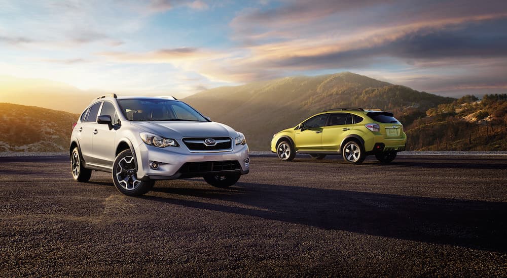 A silver and a green 2015 Subaru Crosstrek are parked in an open area.