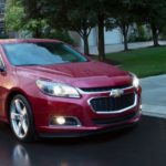 A 2015 Chevy Malibu, popular among used cars, is on a wet road at dusk.