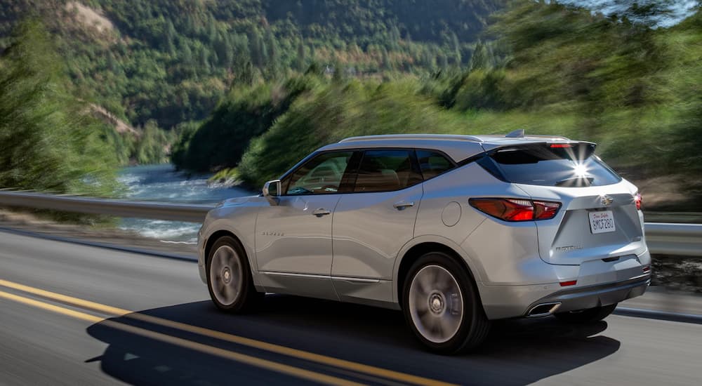 A silver 2019 Chevy Blazer is driving past a river lined with trees.