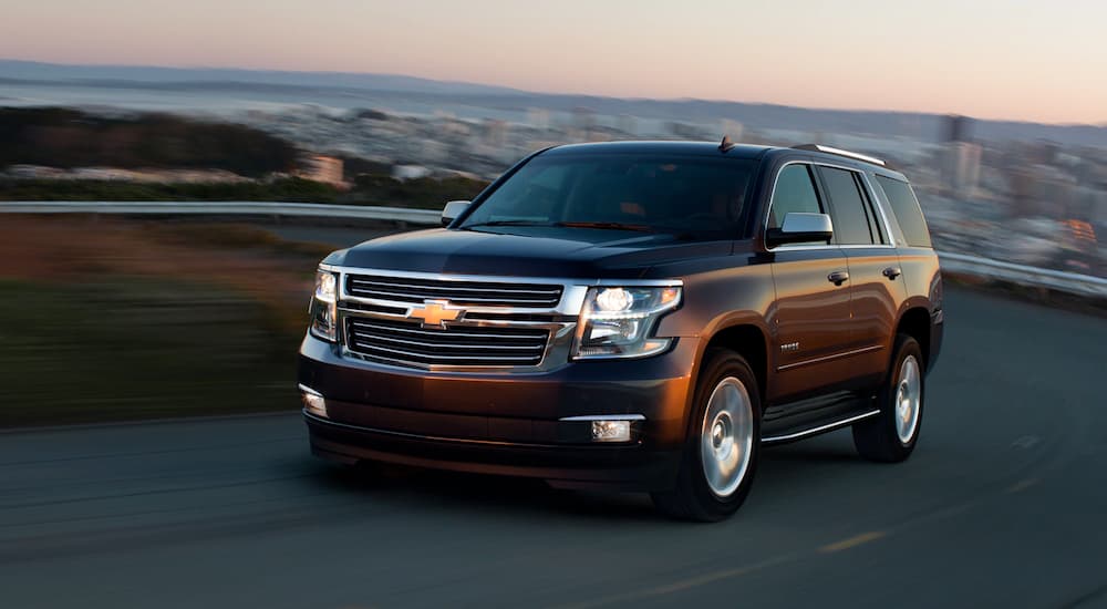 A maroon 2019 Chevy Tahoe is driving away from a city at sunrise.