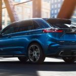 A blue 2019 Ford Edge is driving across a city bridge.