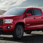 A red 2019 GMC Canyon, which wins when comparing the 2019 GMC Canyon vs 2019 Nissan Frontier, is on a lake shore.