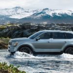 A blue 2020 Kia Telluride is driving through a river in front of mountains.