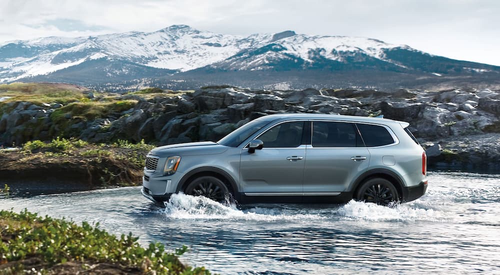A blue 2020 Kia Telluride is driving through a river in front of mountains.