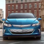 A blue 2019 Chevy Volt is in front of several brick buildings.