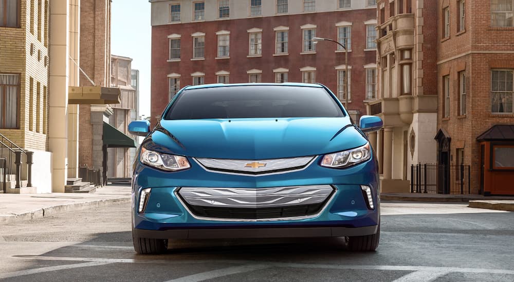 A blue 2019 Chevy Volt is in front of several brick buildings.