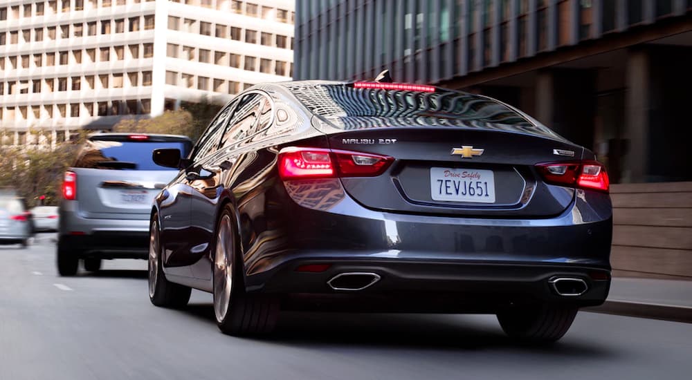 A black Chevy Malibu from the back driving in a city.