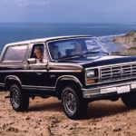 A family is in their black 1983 Ford Bronco in front of the ocean.