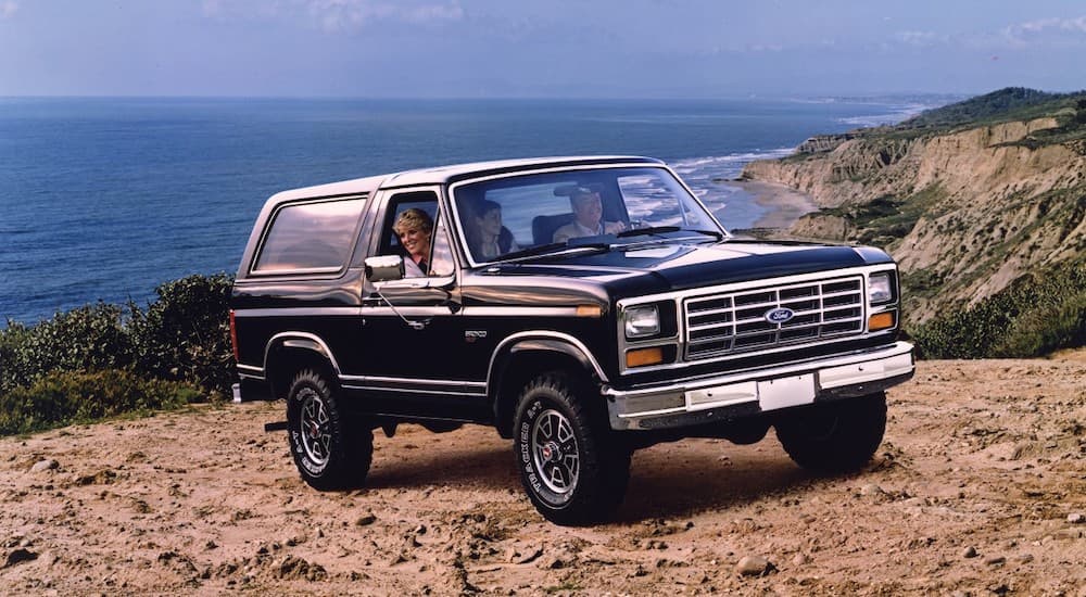 A family is in their black 1983 Ford Bronco in front of the ocean.