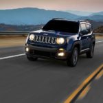 A blue 2016 Jeep Renegade, popular among used cars near me, is driving away from mountains at dawn.