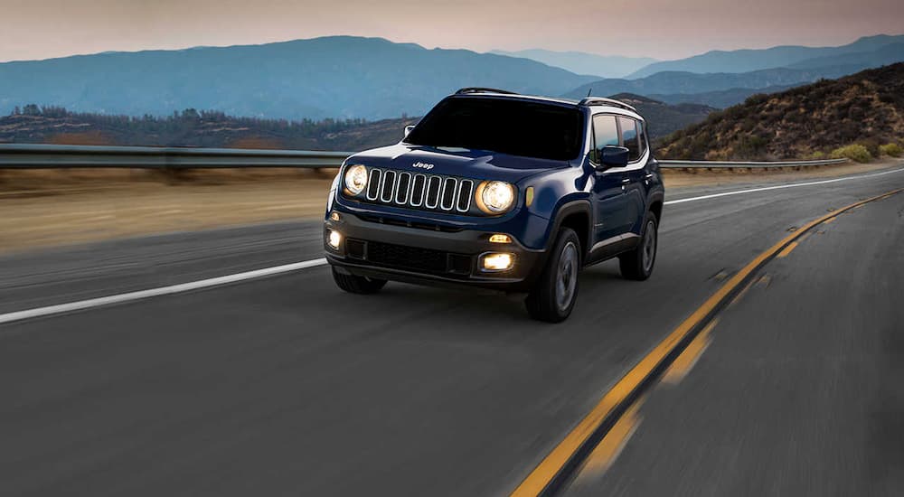 A blue 2016 Jeep Renegade, popular among used cars near me, is driving away from mountains at dawn.