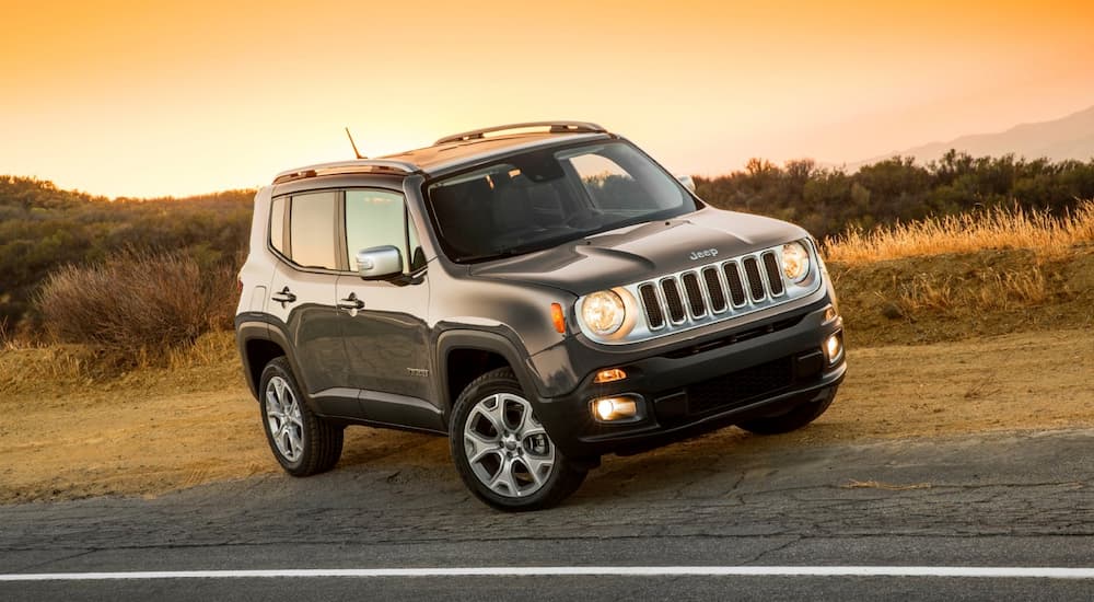 A grey 2016 Jeep Renegade is parked on a desert road with a yellow and orange sky.