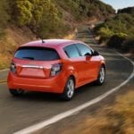 A 2016 Chevy Sonic, which is popular when consumers are buying used cars, is driving on a tree lined highway.