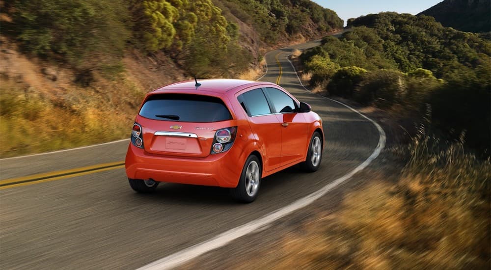 A 2016 Chevy Sonic, which is popular when consumers are buying used cars, is driving on a tree lined highway.