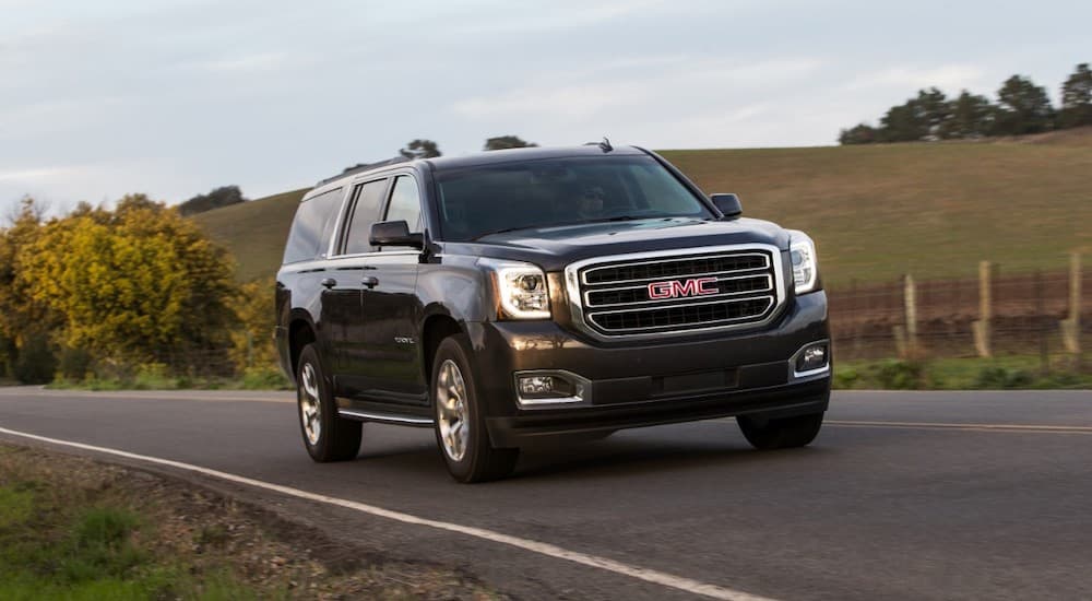 A black 2017 GMC Yukon XL is driving past a field.