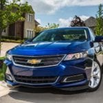 A blue 2016 Chevy Impala is parked in front of a house.