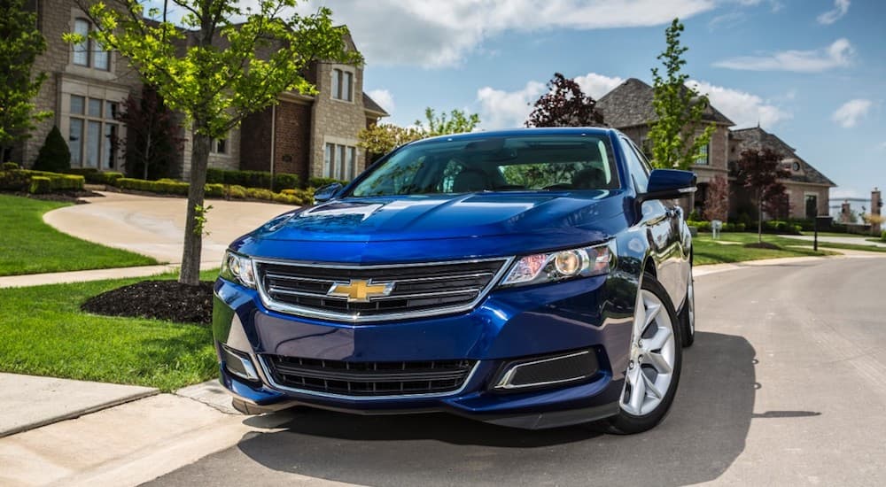 A blue 2016 Chevy Impala is parked in front of a house.